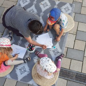 Eine Frau malt mit Kindern auf einem Teppich