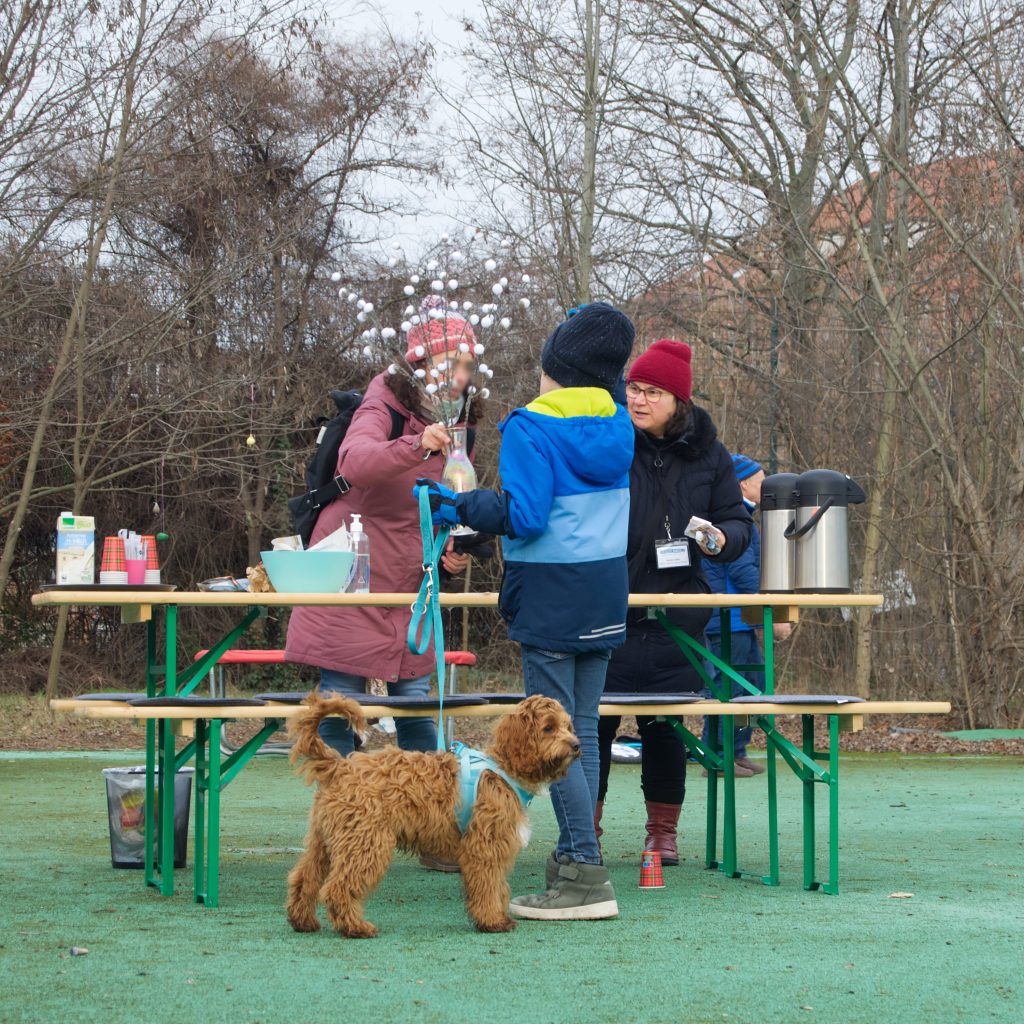 Drei Menschen in Winterkleidung draußen an einem Tisch mit Hund