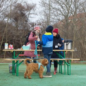 Drei Menschen in Winterkleidung draußen an einem Tisch mit Hund